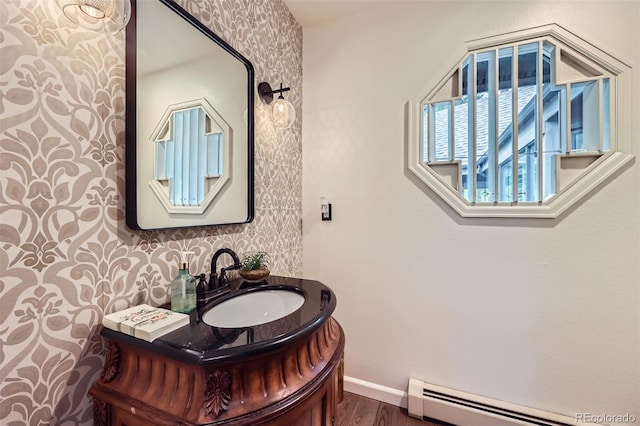 4856 Cheyenne Dr, Larkspur, CO 80118 - bathroom featuring wallpapered walls, baseboard heating, baseboards, wood finished floors, and vanity