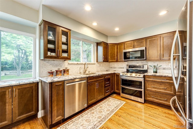 9846 Spring Hill Ln, Highlands Ranch, CO 80129 - kitchen featuring appliances with stainless steel finishes, light stone countertops, backsplash, light wood finished floors, and glass insert cabinets