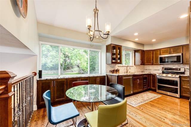 9846 Spring Hill Ln, Highlands Ranch, CO 80129 - kitchen with appliances with stainless steel finishes, a chandelier, tasteful backsplash, light wood-style floors, and light stone counters