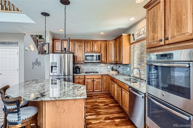 kitchen featuring a center island, sink, decorative light fixtures, stainless steel appliances, and light stone counters