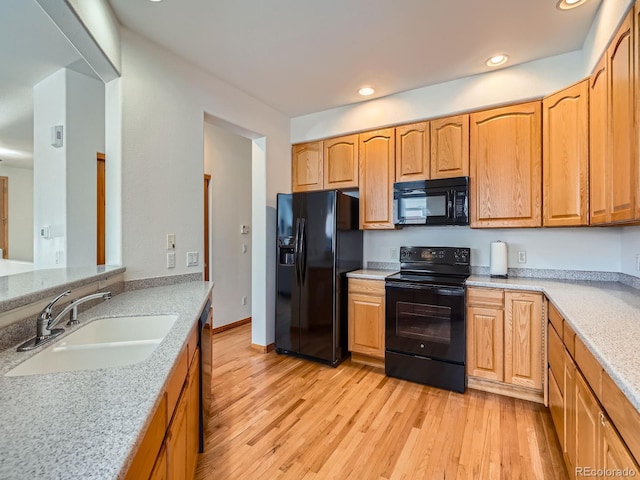 kitchen with light wood-type flooring, light stone countertops, sink, and black appliances