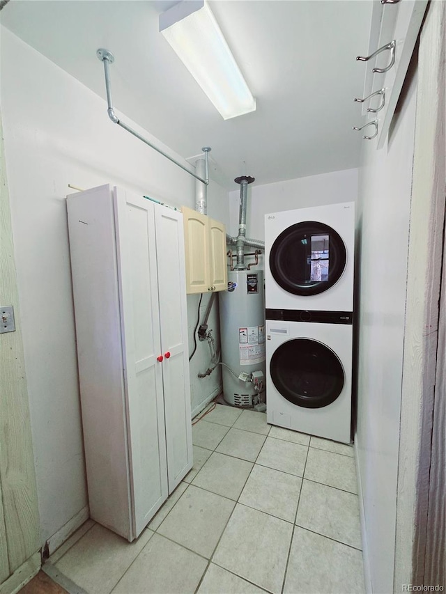 laundry area with light tile patterned flooring, cabinets, stacked washing maching and dryer, and gas water heater