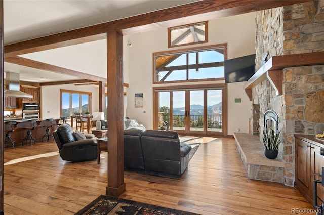 living room featuring beamed ceiling, a healthy amount of sunlight, light wood-type flooring, and a fireplace