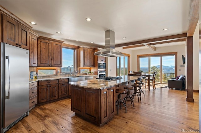 kitchen with island range hood, a kitchen island, appliances with stainless steel finishes, and light hardwood / wood-style flooring