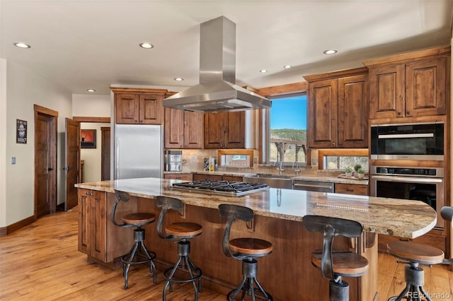 kitchen featuring light stone countertops, stainless steel appliances, a spacious island, and island range hood