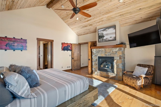 bedroom featuring ceiling fan, wood-type flooring, wooden ceiling, beamed ceiling, and a stone fireplace