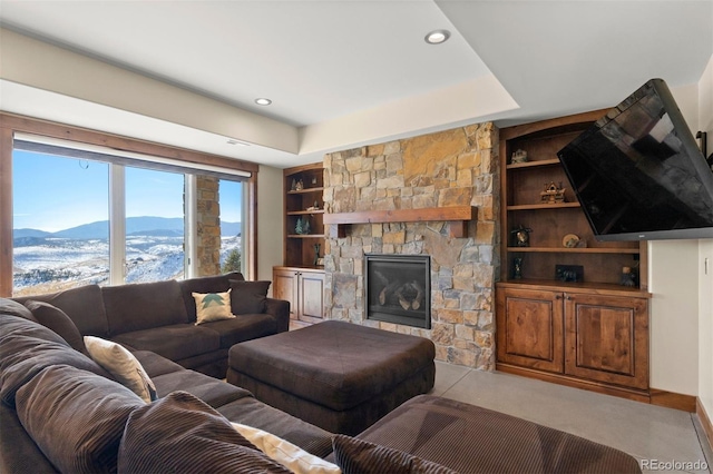 living room with built in shelves, light colored carpet, a raised ceiling, a mountain view, and a stone fireplace