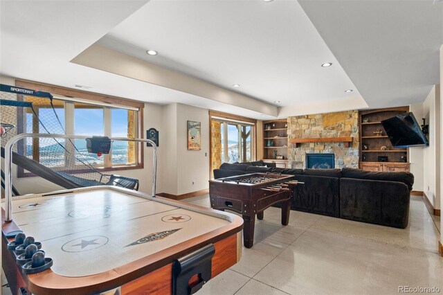 playroom featuring built in features, a raised ceiling, and a stone fireplace