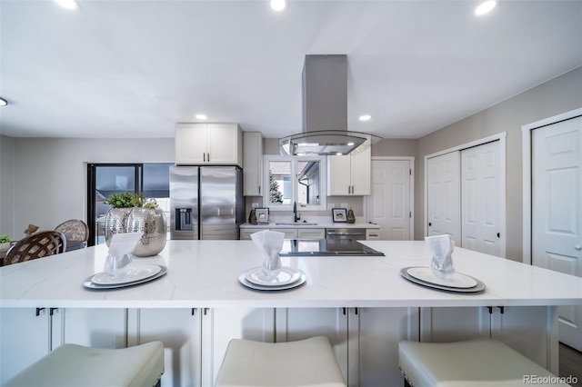 kitchen featuring stainless steel fridge with ice dispenser, a kitchen breakfast bar, island exhaust hood, a large island, and white cabinets