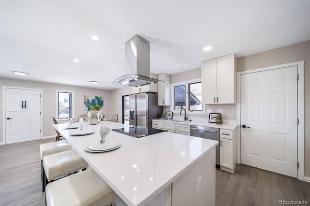 kitchen featuring a breakfast bar, appliances with stainless steel finishes, white cabinetry, a center island, and island exhaust hood