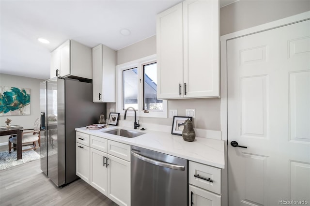 kitchen featuring sink, light stone counters, light wood-type flooring, stainless steel appliances, and white cabinets