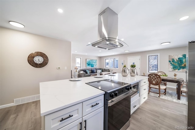 kitchen featuring white cabinetry, island exhaust hood, electric range oven, and light hardwood / wood-style flooring