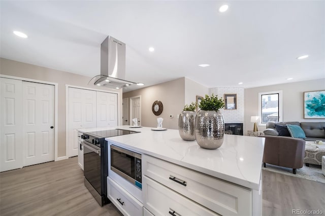 kitchen featuring light stone counters, island range hood, electric range oven, light hardwood / wood-style floors, and white cabinets