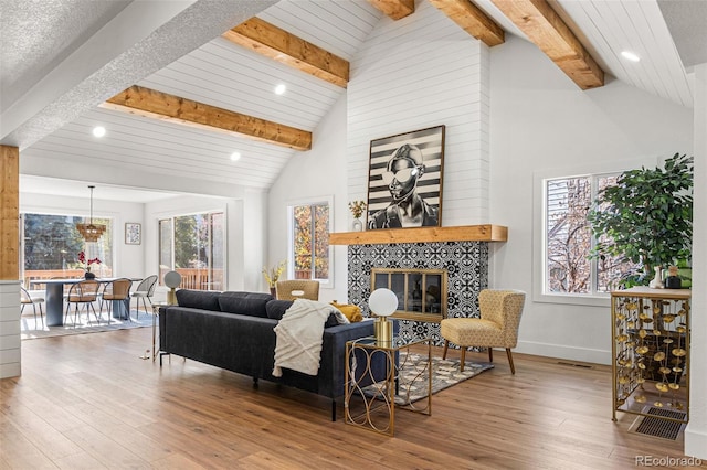 living room featuring high vaulted ceiling, a tiled fireplace, beamed ceiling, and hardwood / wood-style flooring