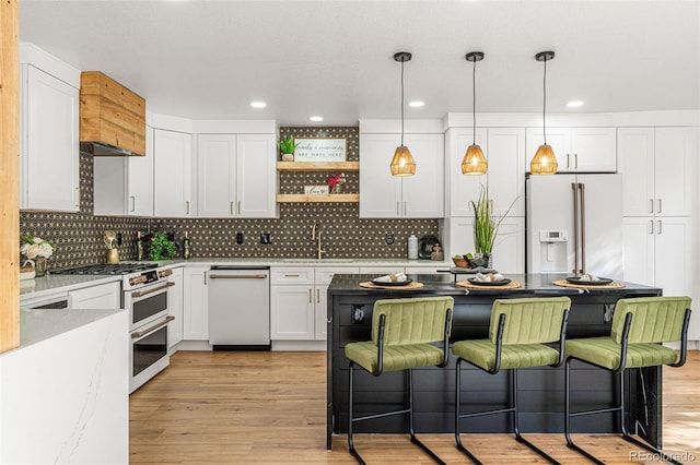 kitchen featuring white cabinets, tasteful backsplash, high quality appliances, pendant lighting, and light hardwood / wood-style flooring