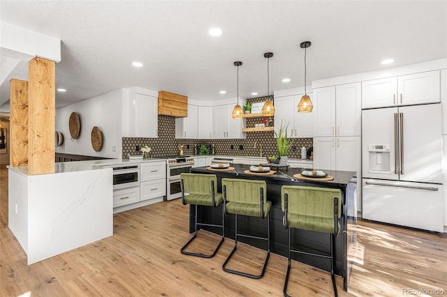 kitchen with light hardwood / wood-style floors, high end appliances, kitchen peninsula, white cabinets, and backsplash