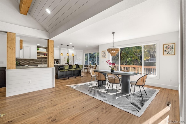 dining space featuring lofted ceiling with beams and light hardwood / wood-style flooring