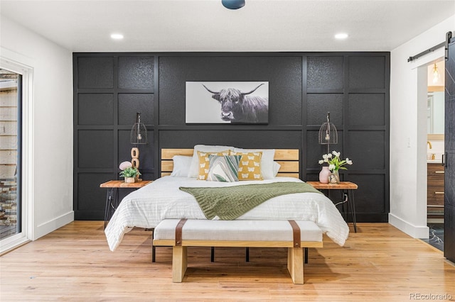 bedroom with a barn door and light wood-type flooring