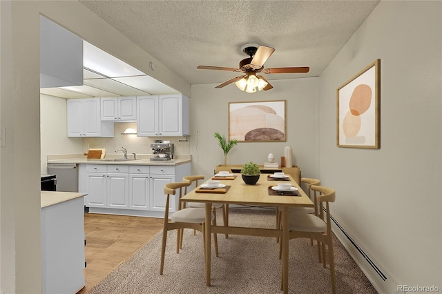 dining room featuring sink, a textured ceiling, light wood-type flooring, a baseboard radiator, and ceiling fan