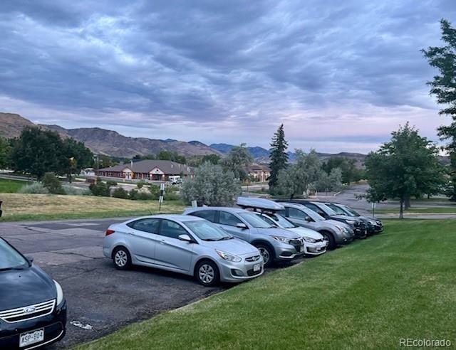 parking at dusk featuring a mountain view and a yard