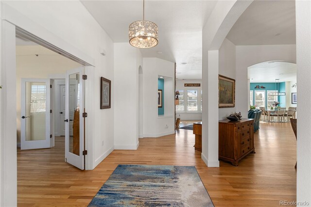 entryway with light wood-style floors, arched walkways, a chandelier, and baseboards