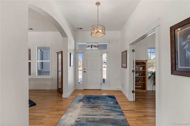 foyer entrance featuring light wood-style floors, baseboards, visible vents, and arched walkways