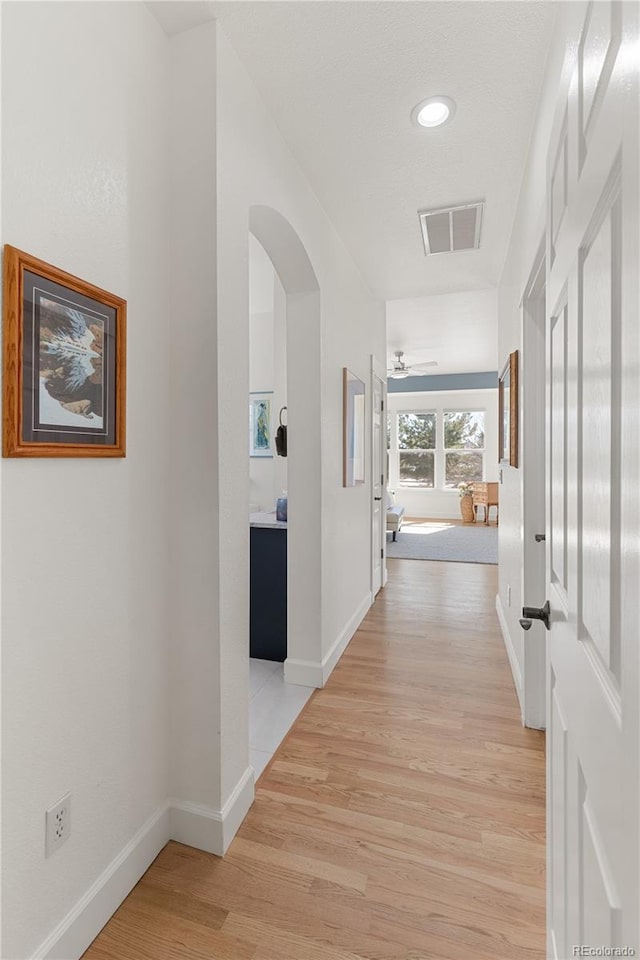 hallway featuring light wood-style floors, baseboards, visible vents, and arched walkways