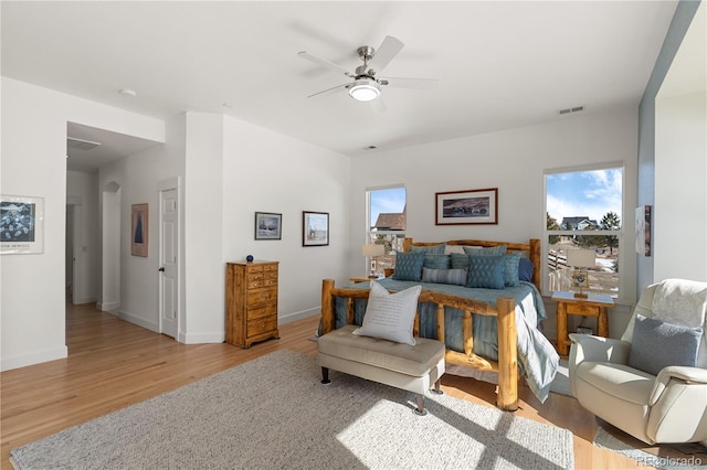 bedroom featuring arched walkways, a ceiling fan, baseboards, visible vents, and light wood-style floors