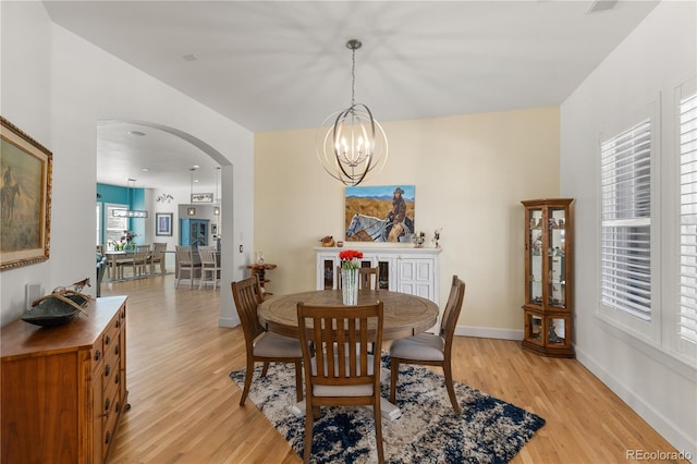 dining space featuring light wood-type flooring, baseboards, arched walkways, and a chandelier