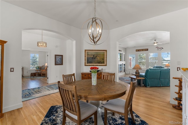 dining area with arched walkways, baseboards, and light wood finished floors