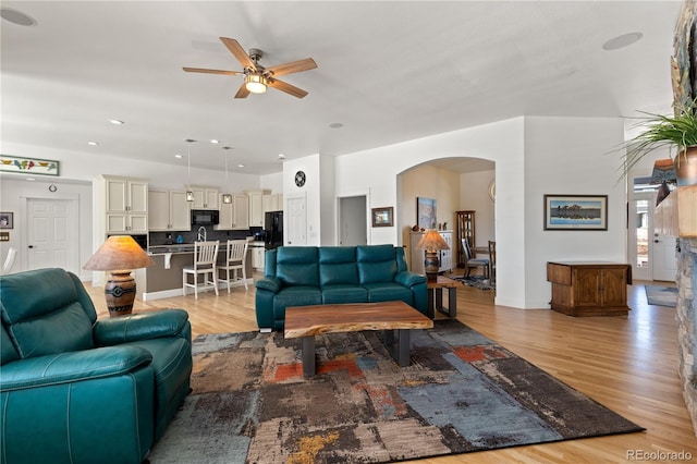 living area featuring light wood-type flooring, ceiling fan, arched walkways, and recessed lighting