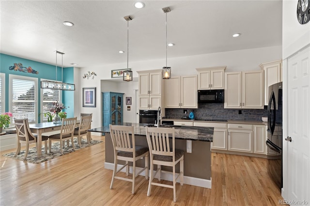 kitchen featuring cream cabinetry, tasteful backsplash, light wood-style floors, a sink, and black appliances