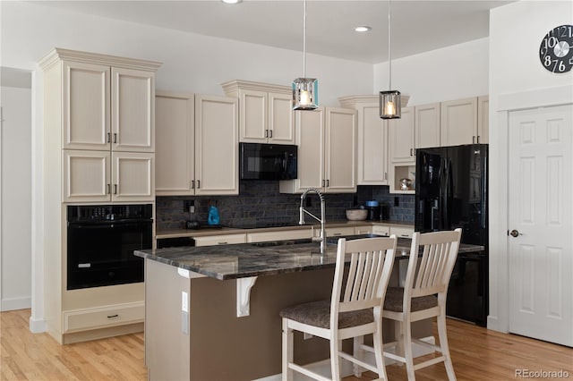 kitchen with tasteful backsplash, cream cabinetry, light wood-style flooring, and black appliances