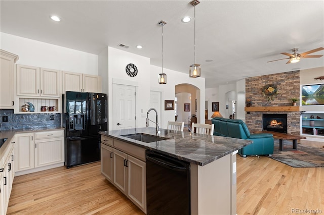 kitchen featuring arched walkways, light wood-style flooring, a large fireplace, a sink, and black appliances