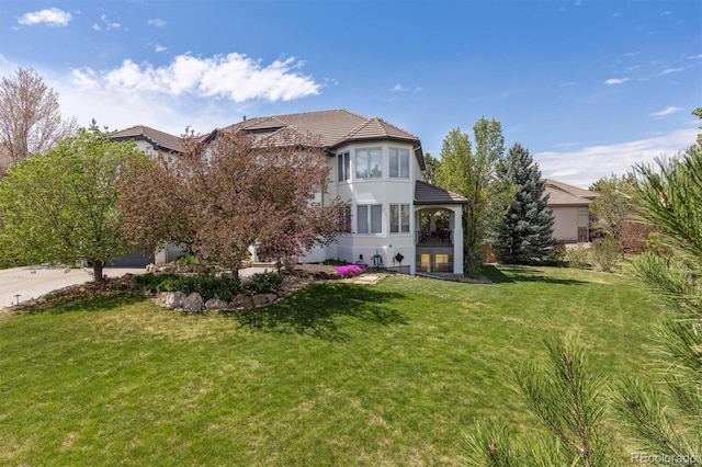 rear view of property with stucco siding, a tiled roof, and a lawn