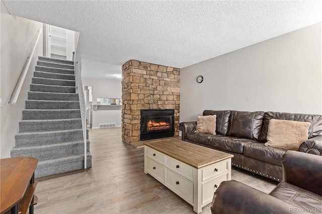 living room featuring a stone fireplace, a textured ceiling, and light wood-type flooring