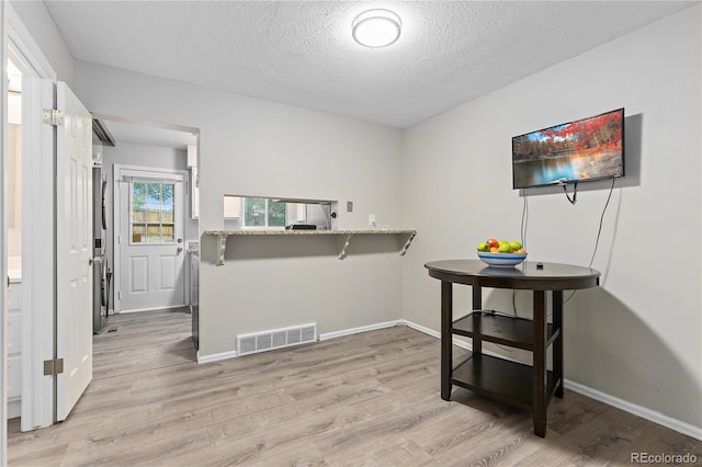 interior space featuring kitchen peninsula, light wood-type flooring, light stone counters, a breakfast bar, and a textured ceiling