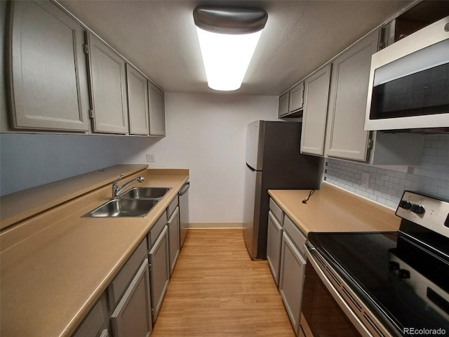 kitchen featuring gray cabinets, sink, backsplash, stainless steel appliances, and light hardwood / wood-style flooring