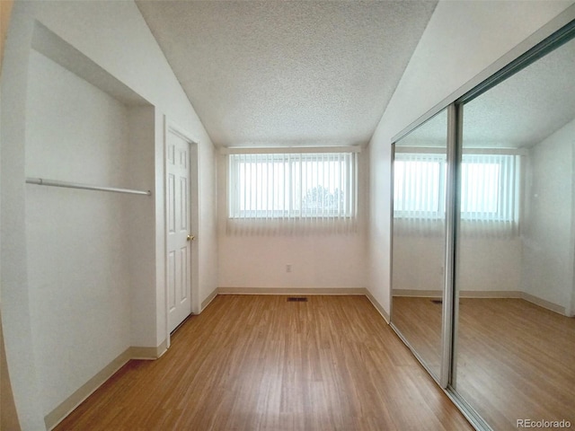 unfurnished bedroom featuring vaulted ceiling, hardwood / wood-style floors, multiple windows, and a textured ceiling