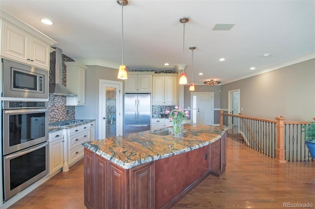 kitchen featuring wall chimney exhaust hood, decorative backsplash, built in appliances, and ornamental molding