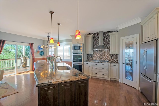 kitchen with appliances with stainless steel finishes, a sink, wall chimney range hood, light stone counters, and wood finished floors