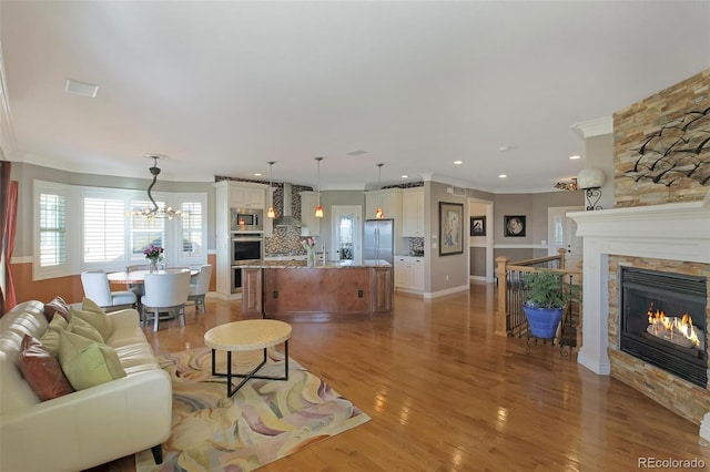 living room featuring light wood finished floors, crown molding, a fireplace, and an inviting chandelier