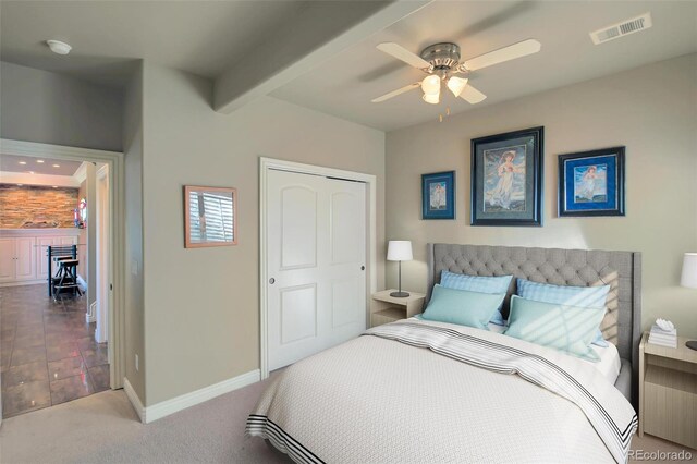carpeted bedroom featuring a ceiling fan, a closet, visible vents, baseboards, and beamed ceiling