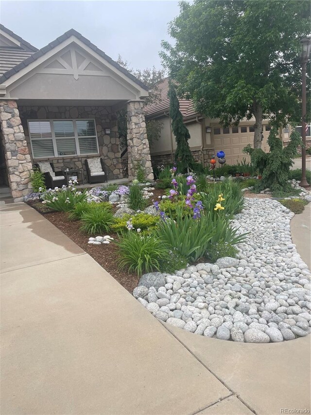 view of front facade featuring stone siding, stucco siding, a garage, and a porch
