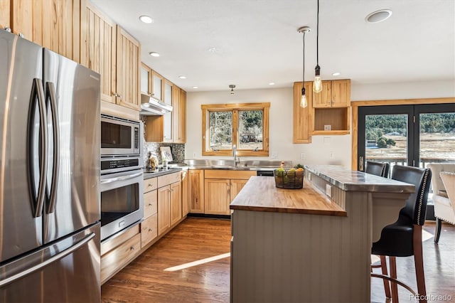 kitchen featuring wood counters, a center island, hanging light fixtures, appliances with stainless steel finishes, and a kitchen breakfast bar