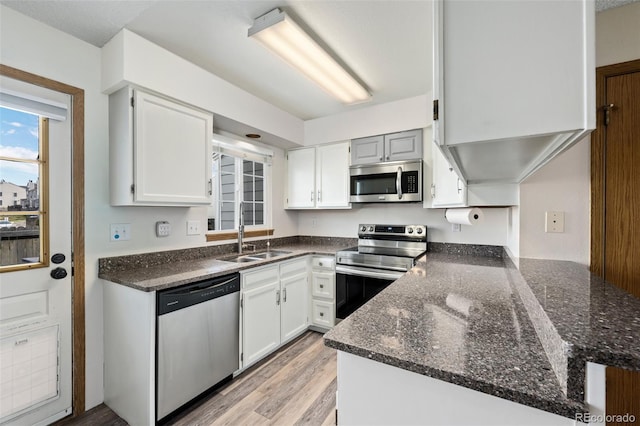 kitchen featuring dark stone countertops, white cabinets, a sink, and appliances with stainless steel finishes