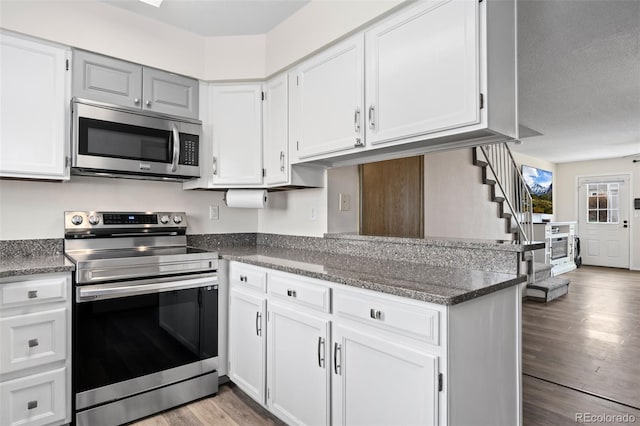 kitchen with a peninsula, white cabinets, dark stone countertops, appliances with stainless steel finishes, and wood finished floors