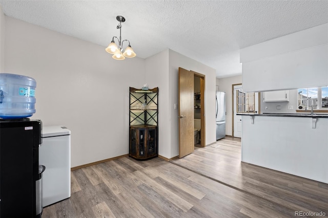 kitchen featuring freestanding refrigerator, an inviting chandelier, light wood-style flooring, a textured ceiling, and dark countertops