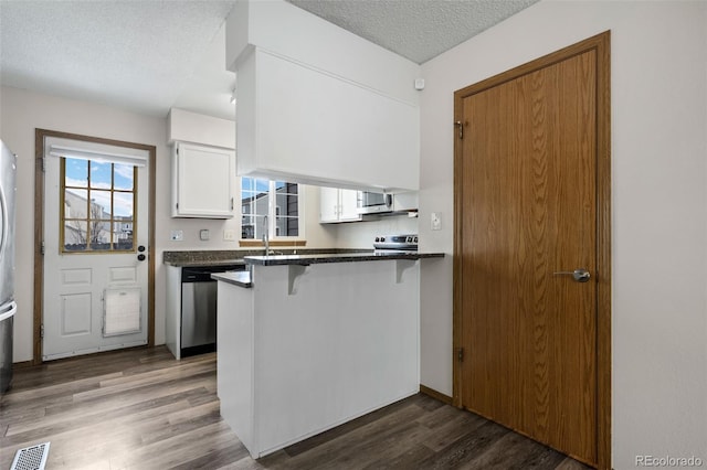 kitchen with visible vents, dark countertops, appliances with stainless steel finishes, white cabinetry, and a breakfast bar area