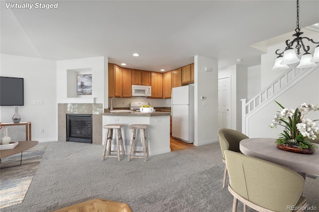 kitchen with white appliances, sink, hanging light fixtures, a breakfast bar area, and light colored carpet